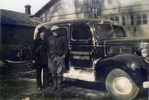 Historiakuva, jossa kaksi miestä poseeraa sähkölaitoksen auton vieressä