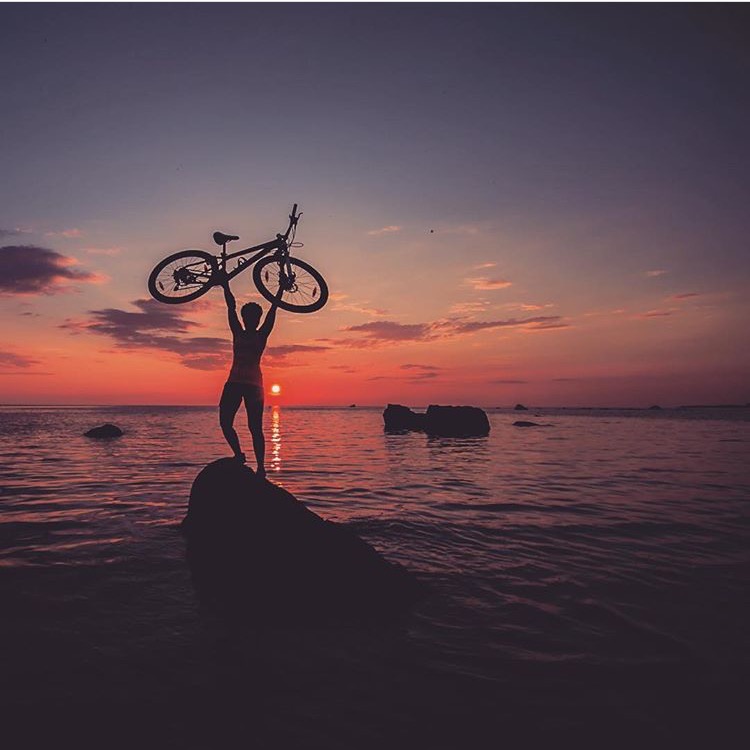 Palkittu kuva, kuvaaja @laizak, julkaistu Instagramissa. Naisen siluetti auringonlaskussa, pitelee pyörää pään päällä.