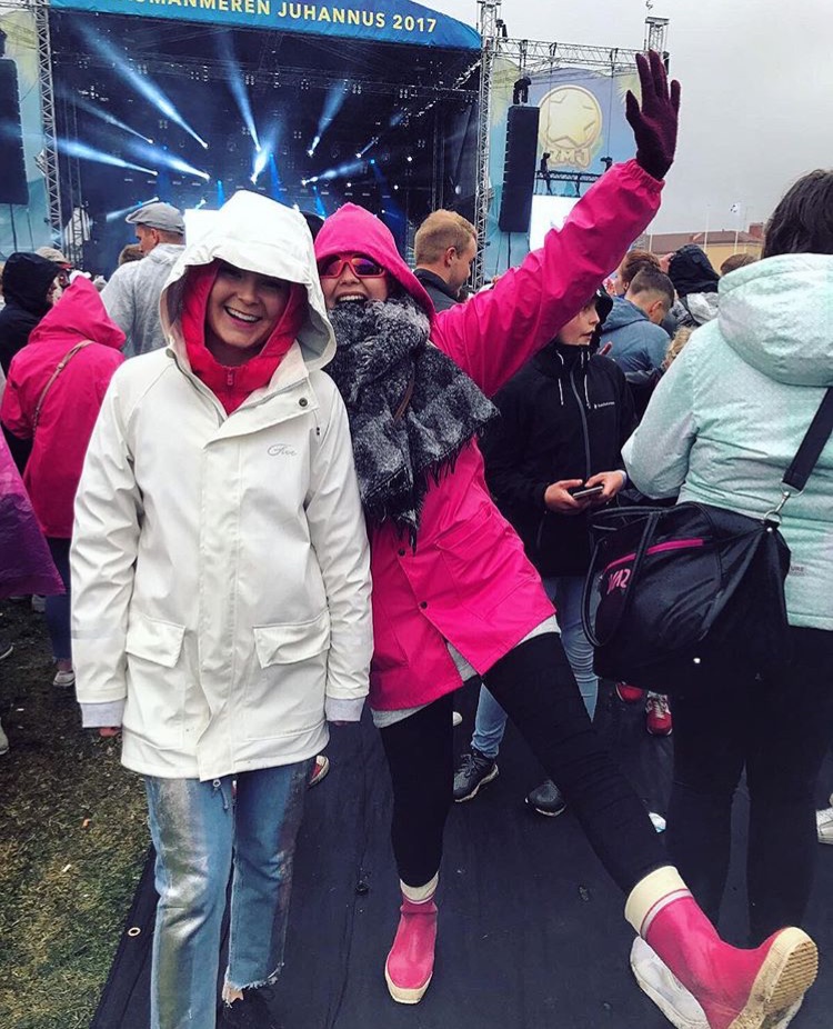 palkittu kuva, kuvaaja @suskuu, kuva julkaistu Instagramissa. Naiset hymyilevät sadevaatteissa festariyleisön joukossa